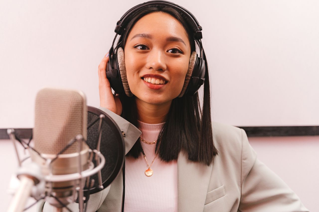 Crafting Captivating Headlines: Your awesome post title goes here Smiling woman in a studio wearing headphones and speaking into a microphone for a podcast.